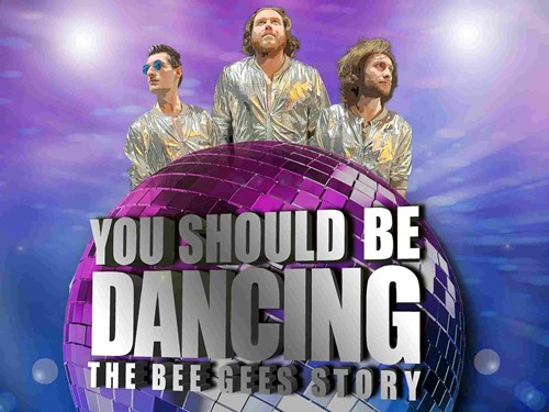 A large disco ball is in the centre of the image with the show title ' You Should Be Dancing – The Bee Gees Story' in bold silver lettering. Behind the disco ball are the performers, they are wearing shiny, silver jackets.