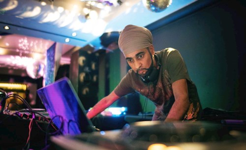 Bhanga DJ extraordinaire Hardeep Sahota looks closely at a laptop with headphones around his neck. 